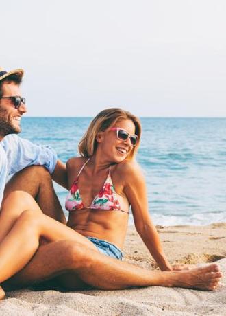 Coppia felice in spiaggia, sole, mare e sorrisi.