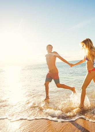Coppia felice corre sulla spiaggia al tramonto, spruzzi d'acqua e gioia.