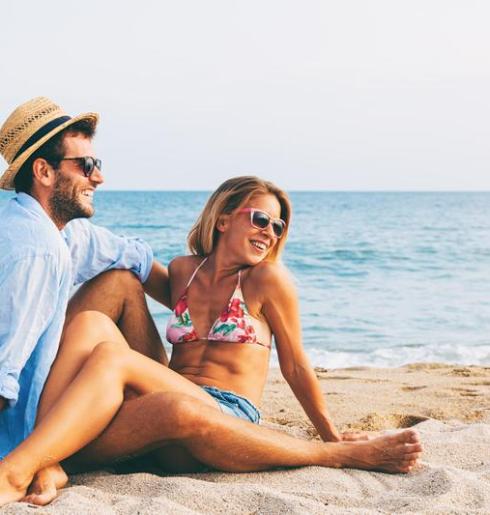 Coppia felice in spiaggia, sole, mare e sorrisi.